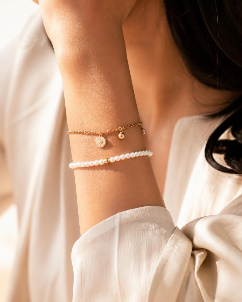 Wrist wearing a gold charm bracelet and a pearl bracelet