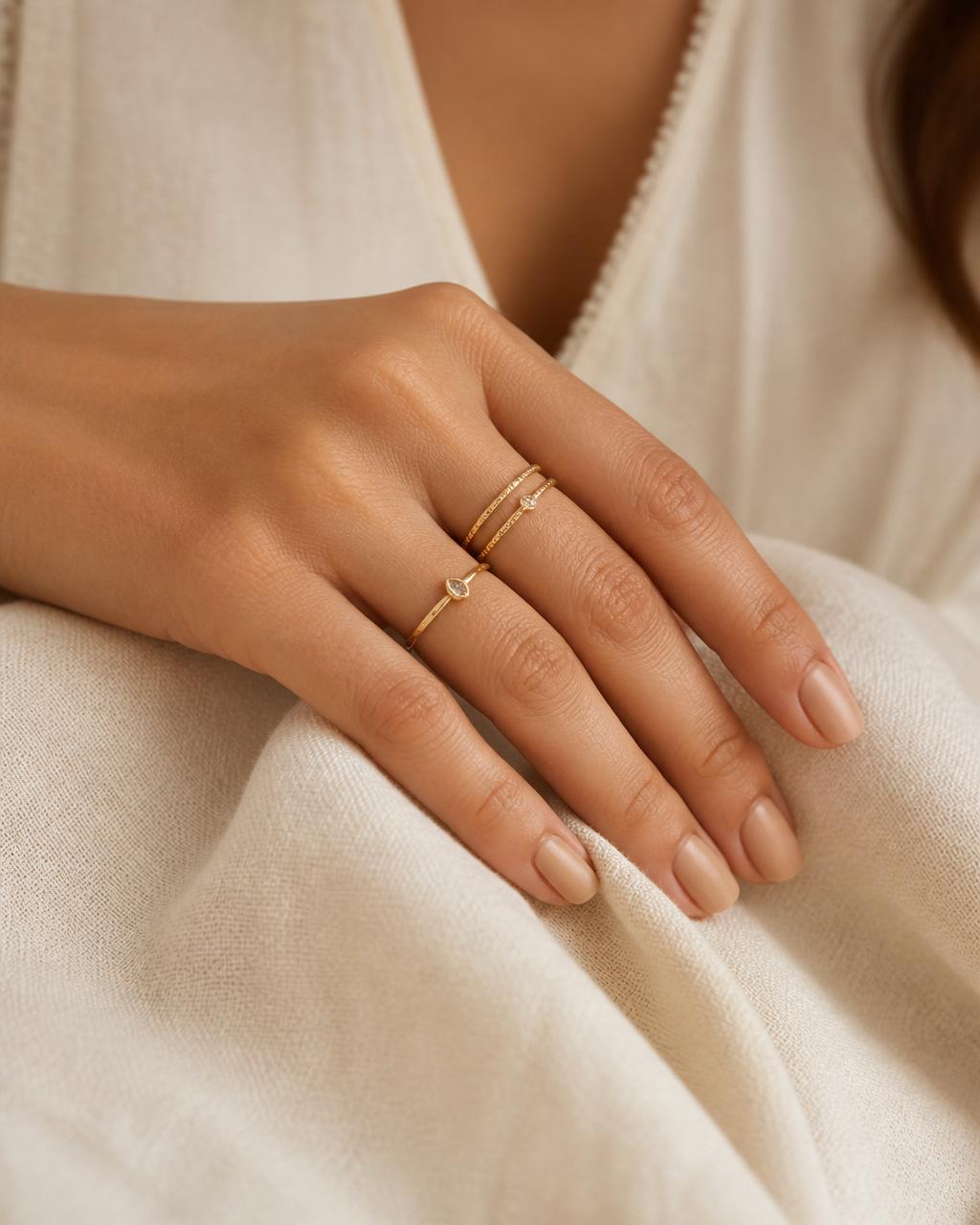Hand with soft neutral manicure wearing slim stacked gold rings